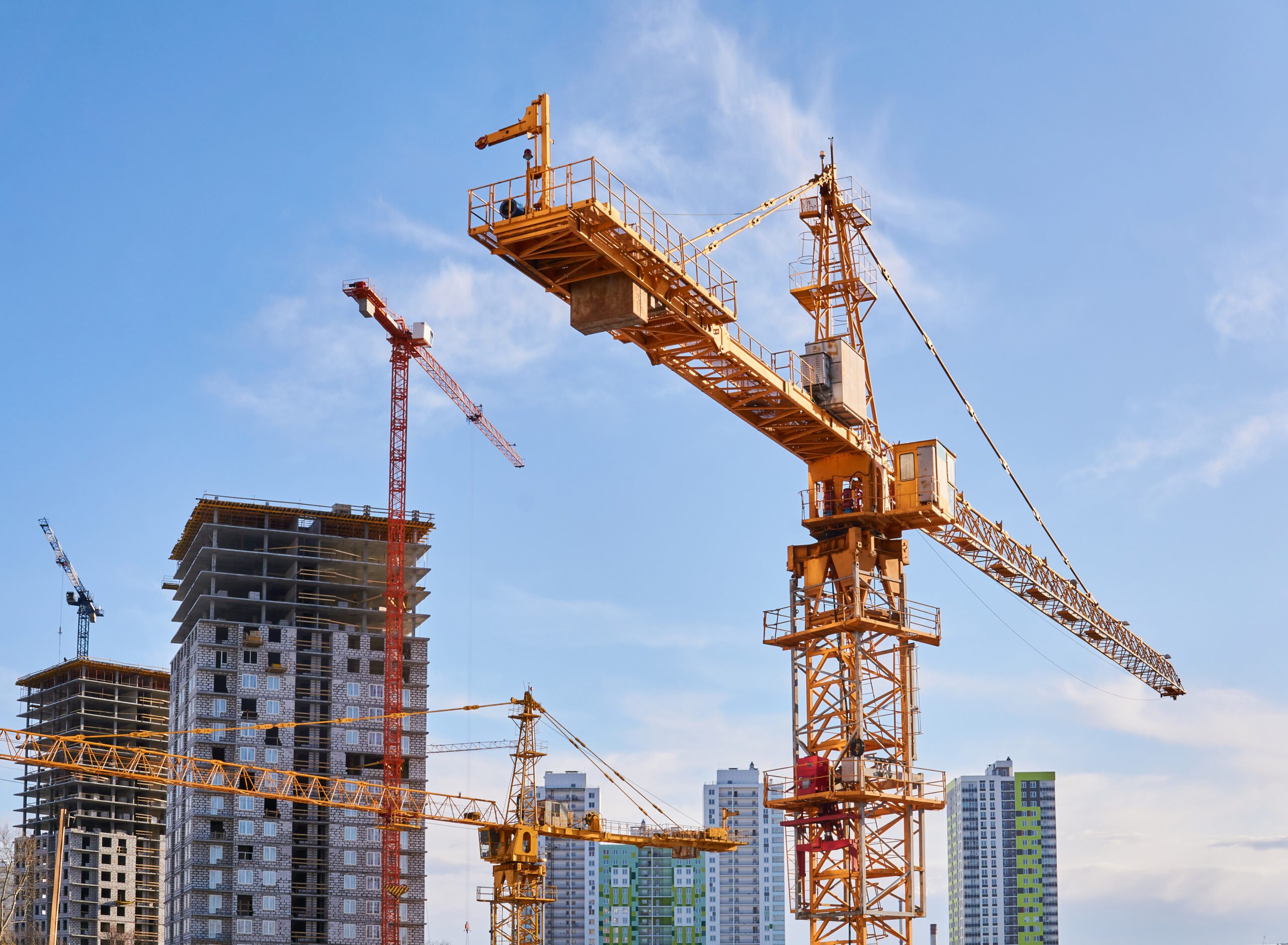 a group of construction cranes in front of a skyscraper.