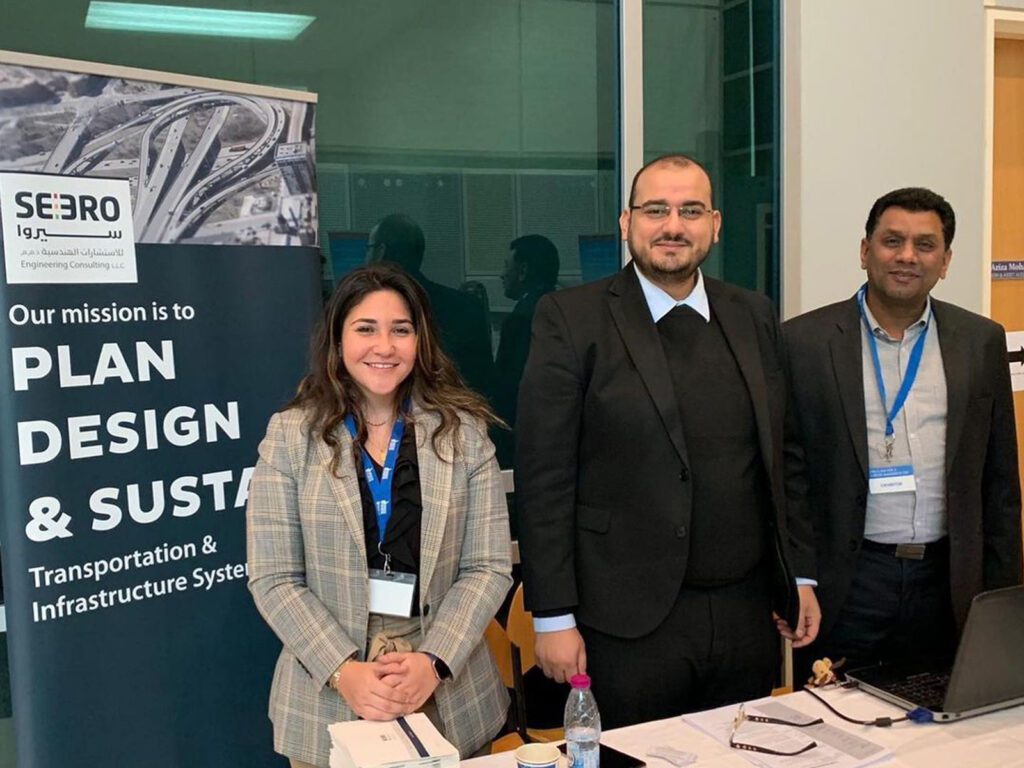 three people standing in front of a table with a plan design and sustainability poster.